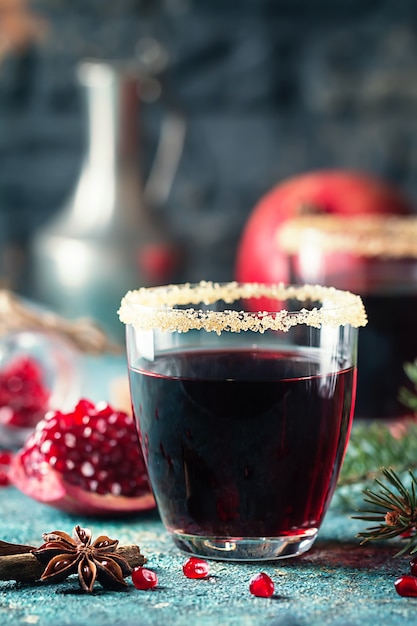 Un verre de jus de grenade avec des fruits de grenade frais et des branches de sapin sur tableau bleu