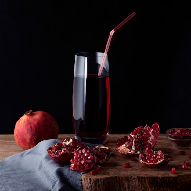 Verre de jus de grenade avec des tranches de grenade et des fruits grenat sur une planche de bois.