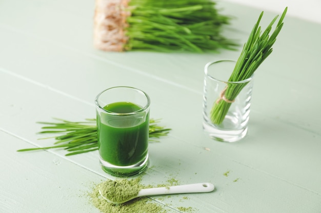 Verre avec jus d'herbe de blé frais et poudre sur bois de couleur