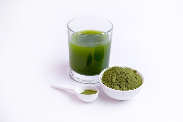 Verre de jus de légumes verts et poudre de légumes sur cuillère à surface blanche