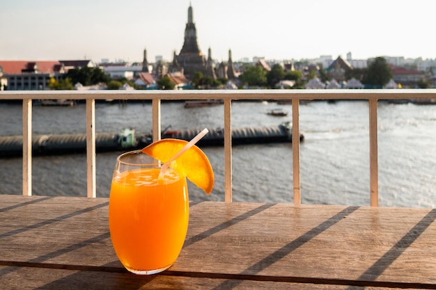 Un verre de jus d'orange est posé sur une table dans un bar sur le toit avec un monument célèbre en arrière-plan. Bangkok, Thaïlande