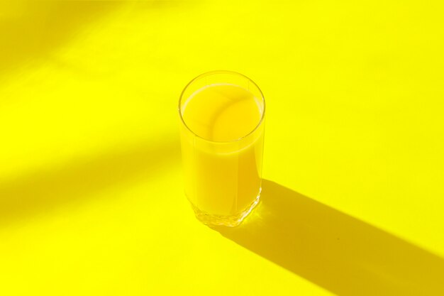 Un verre de jus d'orange sur fond jaune. Concept de vitamines, tropique, été, boisson de soif. Le minimalisme. Lumière naturelle. Mise à plat, vue de dessus.