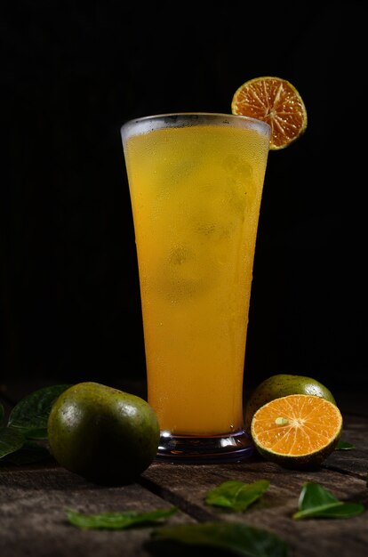 Un verre de jus d'orange fraîchement pressé avec des glaçons sur une table en bois
