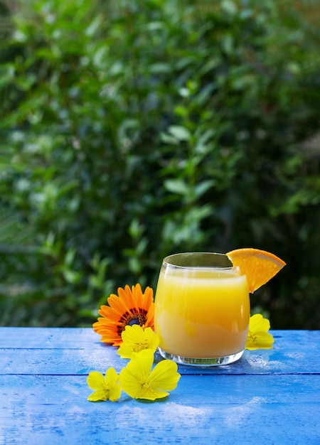 Verre de jus d'orange frais garni d'une tranche d'orange mûre et de fleurs sur la table en bois bleue