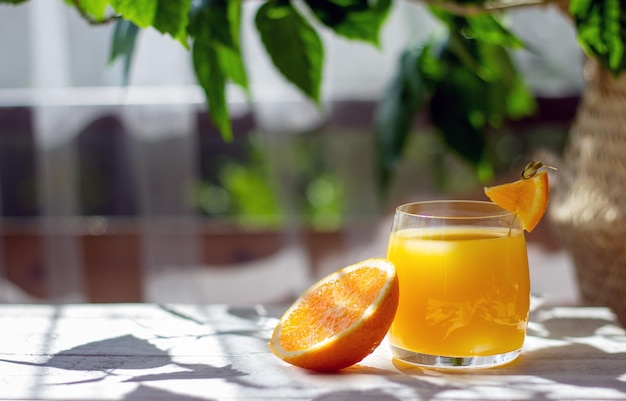 Verre de jus d'orange frais avec des oranges mûres sur la table en bois blanc de la terrasse d'été