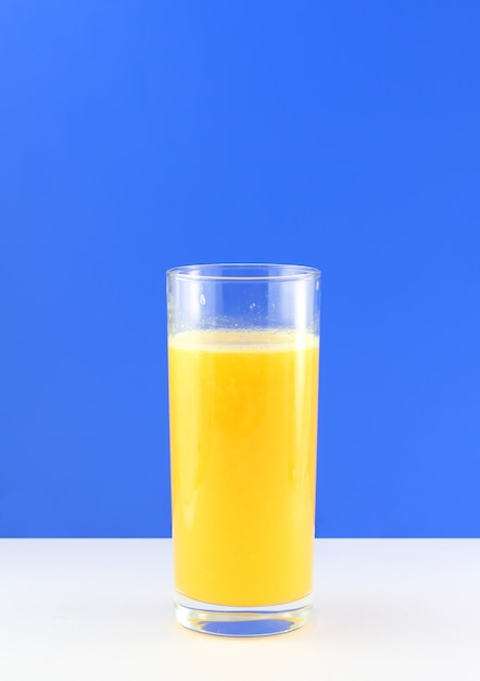 Verre de jus d'orange frais avec une tranche de compression sur fond bleu.