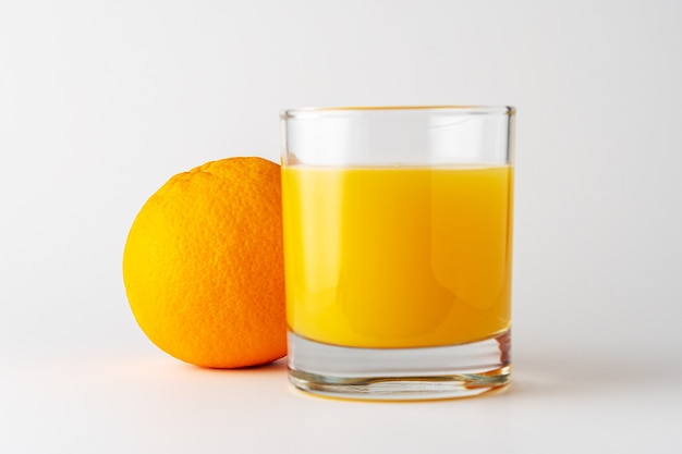 Verre de jus d'orange et fruits orange sur blanc.