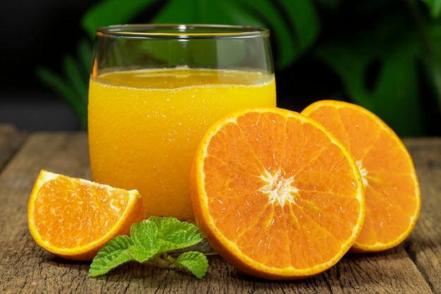 Un verre de jus d'orange et de fruits orange coupés en deux sur la table en bois.