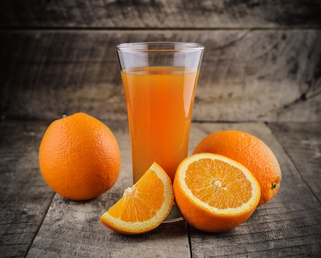 Verre de jus d'orange et oranges fraîches sur bois