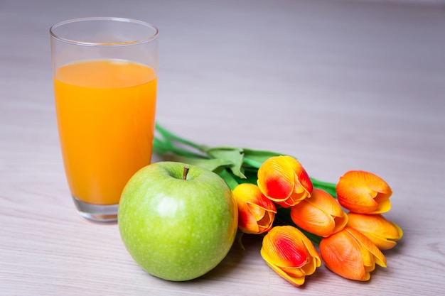 Verre de jus, pomme et tulipes sur table en bois