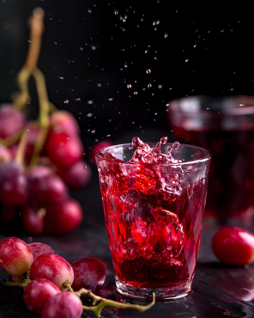 Un verre de jus de raisin frais, mise en conserve de jus de raisin. Fond sombre, éclaboussures et gouttes dans un verre.
