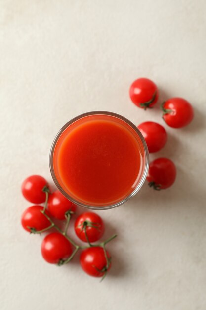 Verre de jus de tomate et tomates sur fond texturé blanc