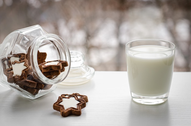 Un verre de lait bio frais avec des biscuits en forme d'étoile sur la fenêtre d'hiver