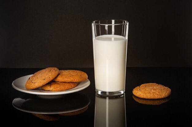 Un verre de lait et biscuits sur table sur fond noir