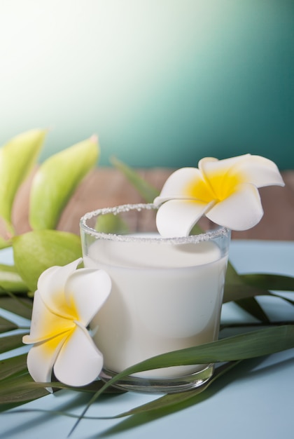 Verre de lait de coco avec fleurs de plumeria et feuille de palmier