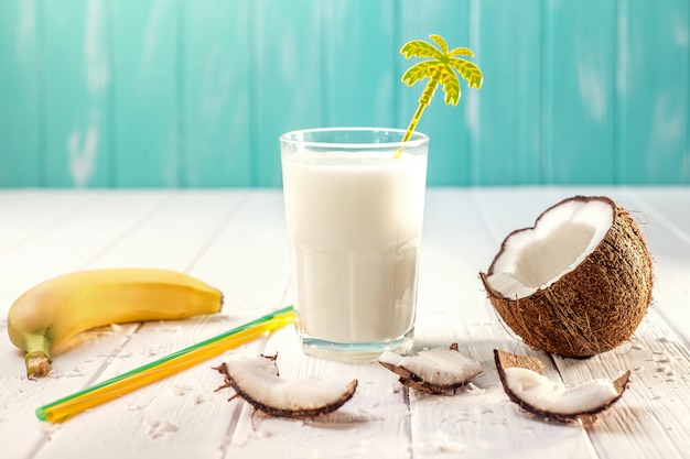 Verre de lait de coco sur une table en bois blanche, bananes. Tropical. Mise au point sélective