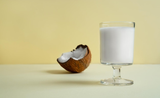 Un verre de lait de coco végétalien et un morceau de noix de coco sur fond jaune clair