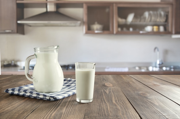 Verre de lait frais et pot sur une table en bois avec cuisine flou comme toile de fond.