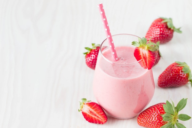 Verre de lait frappé aux fraises, smoothie et fraises fraîches sur fond rose, blanc et bois. Concept d'aliments et de boissons sains.