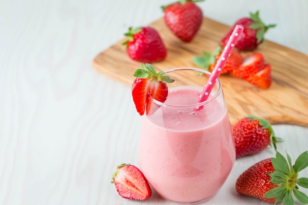 Verre de lait frappé aux fraises, smoothie et fraises fraîches sur fond rose, blanc et bois. Concept d'aliments et de boissons sains.
