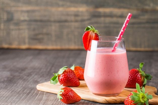 Verre de lait frappé aux fraises, smoothie et fraises fraîches sur fond rose, blanc et bois. Concept d'aliments et de boissons sains.