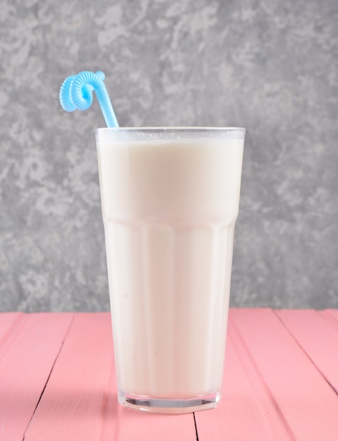 Un verre de lait frappé avec une paille sur une table en bois de couleur pastel