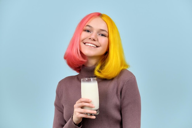 Verre de lait à la main d'un beau modèle adolescent souriant sur fond de studio bleu