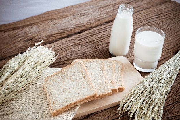 Verre de lait et de pain de blé entier sur la planche de bois