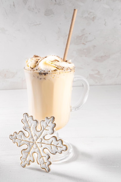 Verre de lait de poule de Noël traditionnel avec crème fouettée et flocon de neige décoratif à la cannelle sur blanc