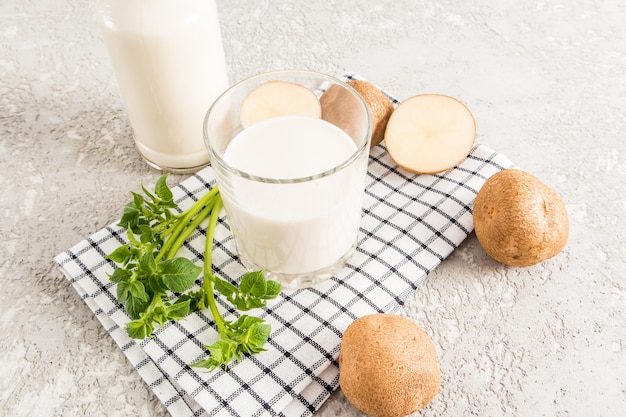 Un verre de lait végétal de tubercules de pomme de terre sur une serviette en tissu et un fond de béton gris avec des tubercules de pomme de terre et une bouteille de lait