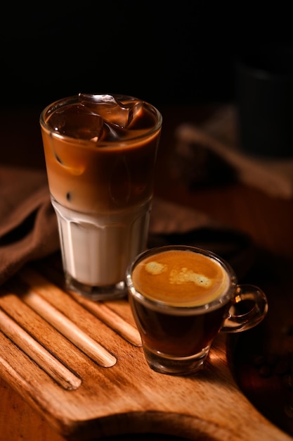 Un verre de latte glacé et un expresso chaud sur une planche de bois rustique sur fond sombre