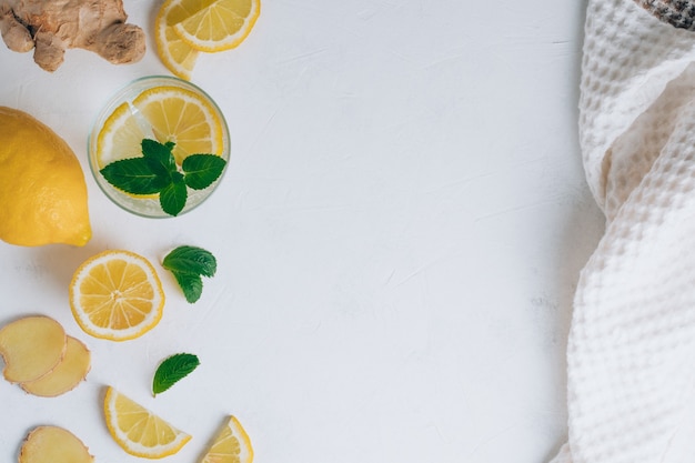 Verre avec limonade et ingrédients pour la cuisson. Gingembre, citron, menthe et serviette sur une surface blanche. Mise à plat. Espace de copie