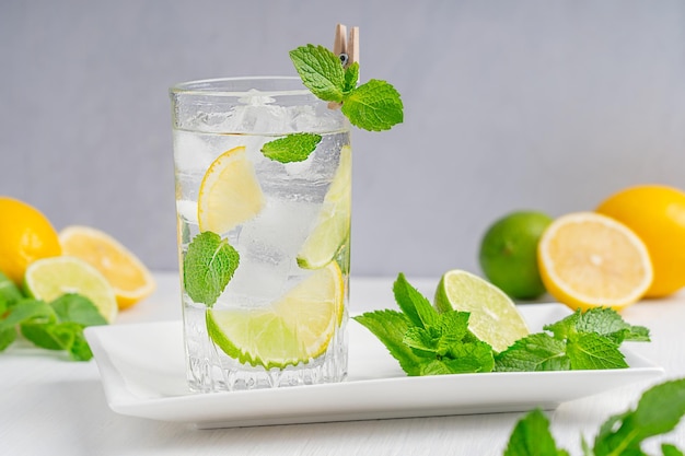 Verre de limonade rafraîchissante froide faite de tranches de citron vert et de citrons, de glace, de feuilles de menthe et de soda sur table