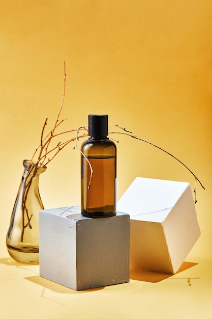 Verre maquette bouteille de shampoing ou revitalisant de produits cosmétiques pour le corps sur des formes géométriques et une branche séchée. Concept de beauté spa cosmétique bio écologique naturel.