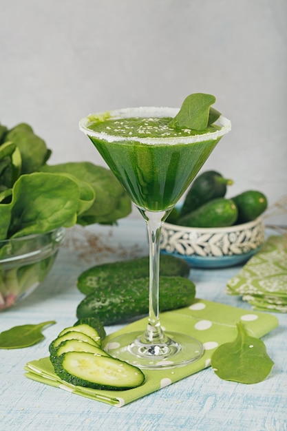 Verre à martini rempli d'épinards verts frais et de smoothie au concombre sur fond de bois bleu clair. Boissons non alcoolisées. Alimentation saine et concept végétarien.