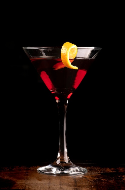 Verre à martini vue de face avec une tranche d'orange et une boisson aux cerises sur fond sombre sur une table en bois