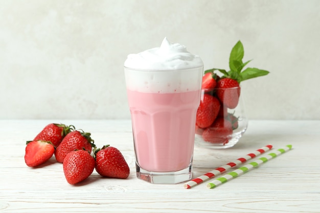 Verre de milk-shake aux fraises et ingrédients sur table en bois blanc