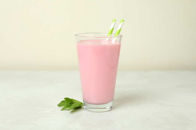 Verre de milkshake aux fraises sur une table texturée blanche