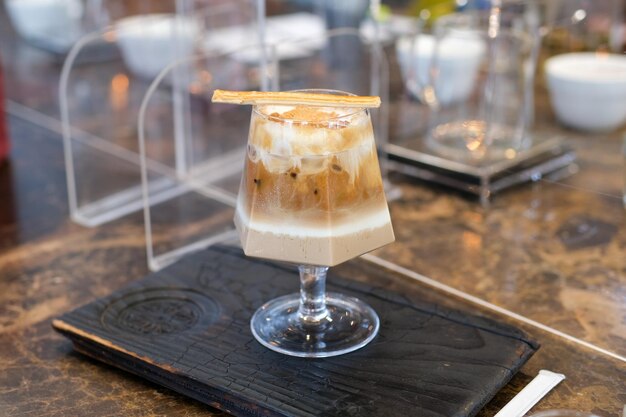 Verre de mise au point sélective de café glacé avec sirop de caramel au lait dans un café café au lait froid dans une tasse sur une table en bois dans un café avec fond de lumière du soleil