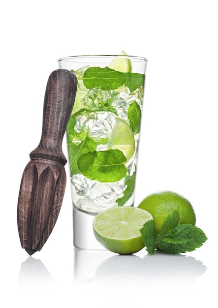 Verre de Mojito cocktail alcoolisé d'été avec des glaçons menthe et citron vert sur fond blanc avec citron vert cru et presse-agrumes en bois