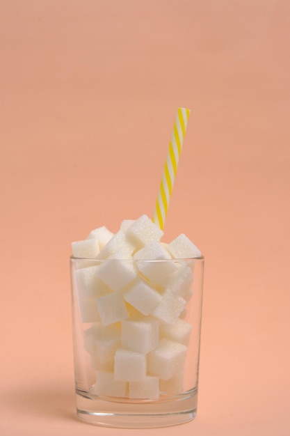 Verre avec morceaux de sucre raffiné et tube à boire sur fond beige