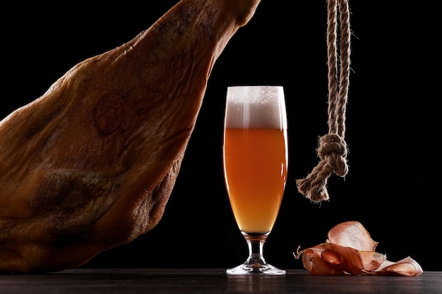 Un verre de mousse de bière légère, jambe, jambon de Parme. Sur fond noir. Place pour le logo.