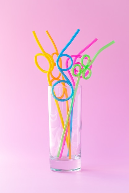 Verre avec de nombreuses pailles à cocktails colorées en plastique sur fond rose, concept d'humeur amusant. Abstraction, design concis créatif.