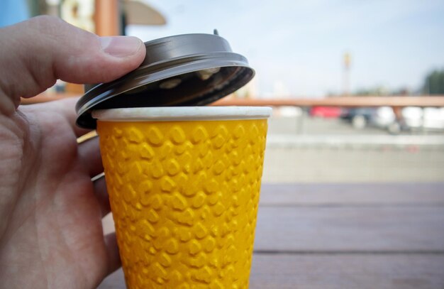 Photo un verre de papier jaune de thé ou de café à emporter sur une table dans un café une main couvre un