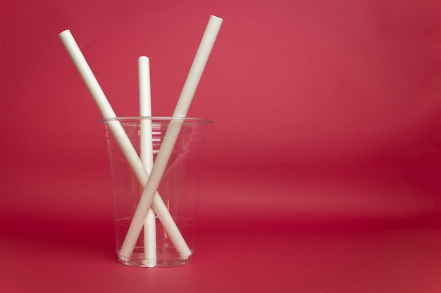 Verre en plastique vide avec de la paille de papier isolé sur fond rouge.