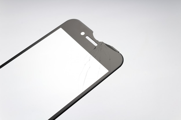 Verre de protection fissuré pour smartphone sur fond blanc.