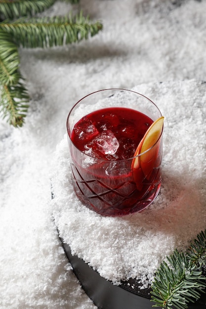 Verre de punch rouge ou cocktail rouge avec de la glace dans la neige avec un sapin de Noël