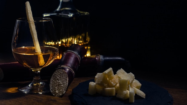 Verre de rhum de canne avec des morceaux de canne sur une table en bois rustique et fond sombre