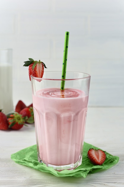 Un verre de smoothie au lait de fraise. Smoothie sain aux fraises dans un verre avec des baies. Cocktail de protéines avec du sirop de fraise, des baies et des pailles à cocktail en papier vert.