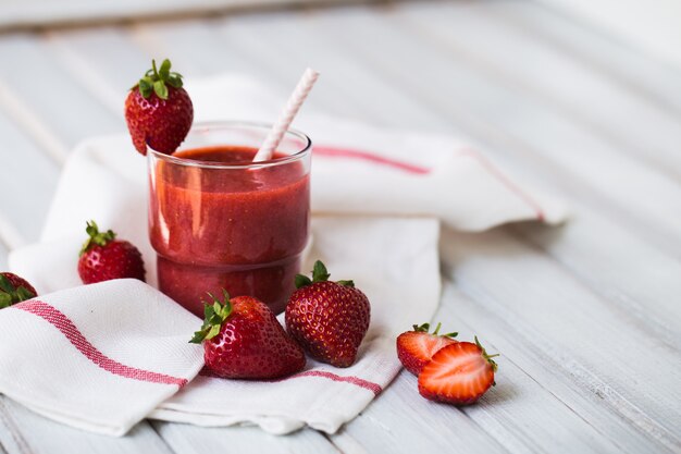 Un verre de smoothie aux fraises sur un fond en bois blanc